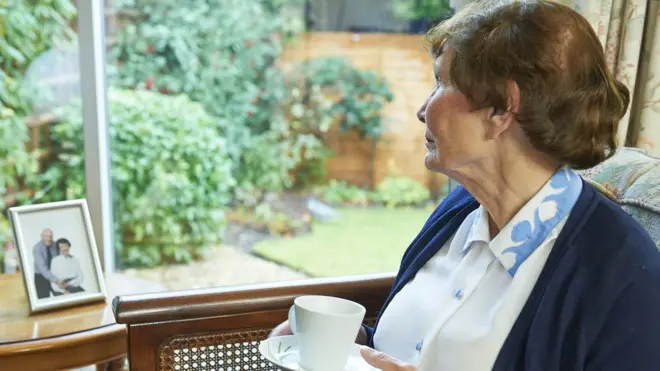 Žena gleda kroz prozor držeći šolju čaja