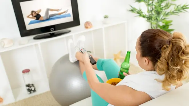 Una mujer viendo un programa deportivo con una bebida en la mano