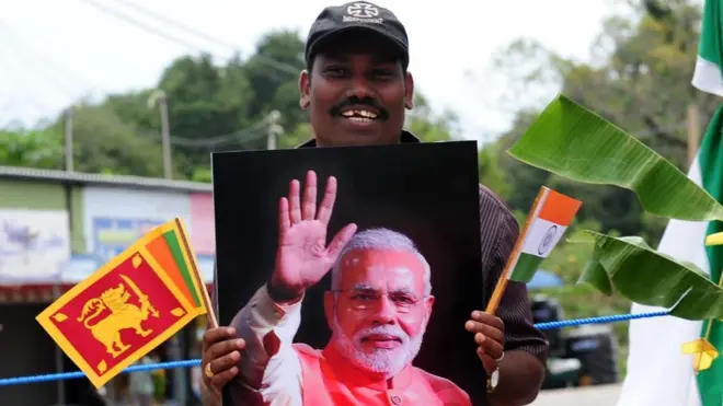 A Sri Lankan ethnic Tamil holds memorabilia bearing the portrait of Indian Prime Minister Narendra Modi as he waits for his arrival in a ceremony to hand over Indian-funded houses to Tamils displaced or made destitute by fighting in Jaffna, some 400 kilometres (250 miles) north of Colombo on March 14, 2015. Narendra Modi landed in Jaffna on March 14, becoming the first Indian prime minister to visit Sri Lanka's war-ravaged northern Tamil heartland. AFP PHOTO / Lakruwan WANNIARACHCHI (Photo credit should read LAKRUWAN WANNIARACHCHI/AFP/Getty Images)