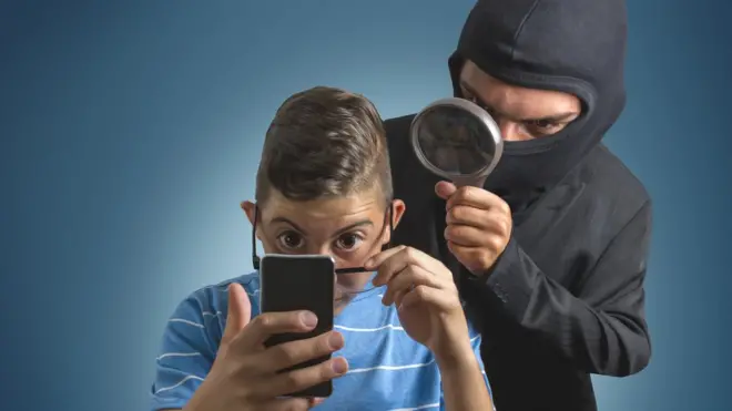 Niño mirando datos en un celular y un ladrón detrás.