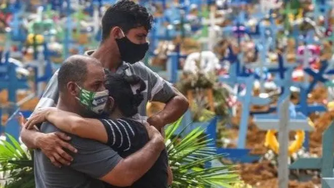 رجل يعانق امرأة وكل منهما يرتدي كمامة وسط مقبرة