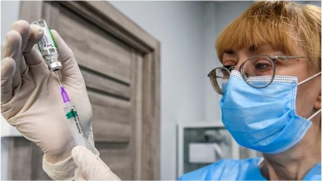 A medical worker in protective masks and gloves removes a dose of the Oxford-AstraZeneca Covishield coronavirus vaccine from a vial at a hospital in Kyiv, Ukraine, in April 2021