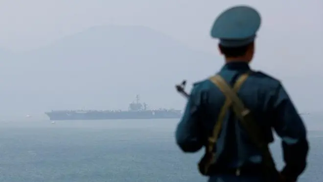 Một người lính Việt Nam, phía xa là hàng không mẫu hạm Hoa Kỳ USS Carl Vinson sau khi đến cảng Đà Nẵng, hôm 5/3