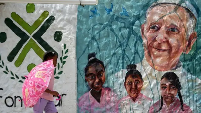 Niña pasa frente a un mural con la cara del papa Francisco en Cartagena de Indias, Colombia.