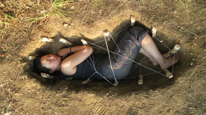 Jae Rhim acostada en la tierra reproduce una forma de entierro ecológico.