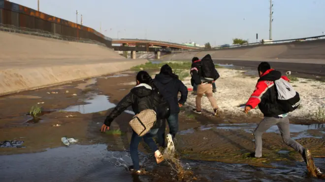 A group of people run at the Rio Bravo, at the Paso del Norte checkpoint, in Ciudad Juarez