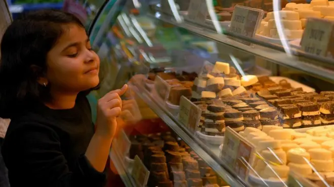 طفلة تنظر إلى أنواع الشوكولاتة في متجر لبيع الحلويات
