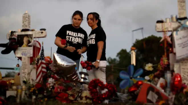 Heather Mesch (C) and her daughter Alexa place roses next to crosses placed in front of the fence of the Marjory Stoneman Douglas High School to commemorate the victims of the mass shooting, in Parkland, Florida, U.S., February 21, 2018