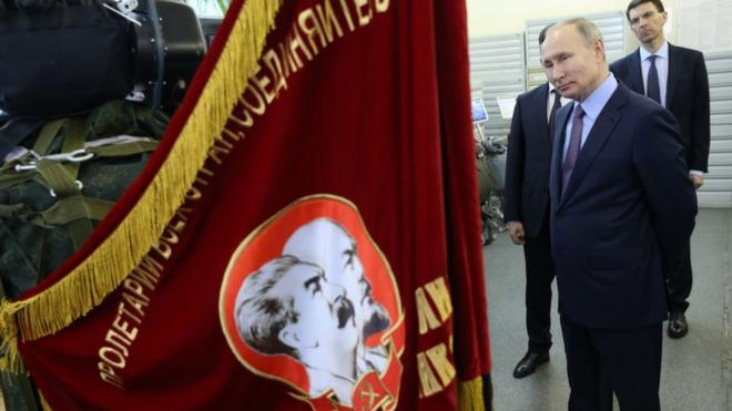 Presidente russo é fotografado ao lado bandeira vermelha com retratos dos líderes soviéticos Vladimir Lenin e Joseph Stalin
