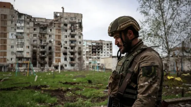 A Ukrainian serviceman walks near a residential building damaged by shelling in the frontline city of Bakhmut