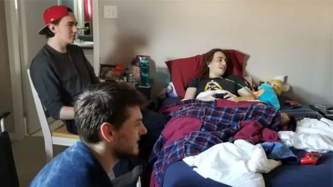 Щасливий геймер, прикутий до ліжка,грає у гру в оточенні друзів.