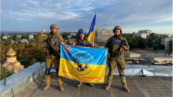 Ukrainian soldiers hold a flag at a rooftop in the town of Kupiansk