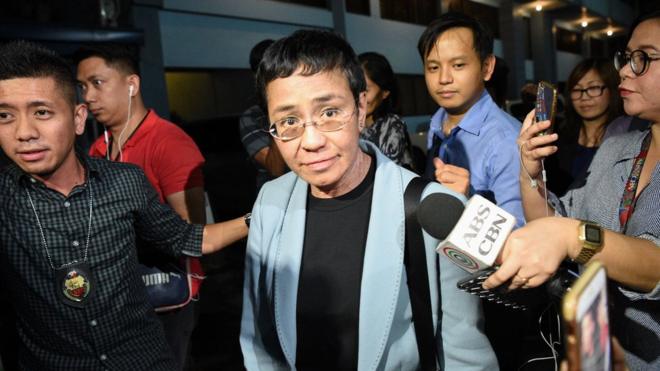 Philippine journalist Maria Ressa (C) is surrounded by the press as she is escorted by a National Bureau Investigation (NBI) agent (L) at the NBI headquarters after her arrest in Manila on February 13, 2019.