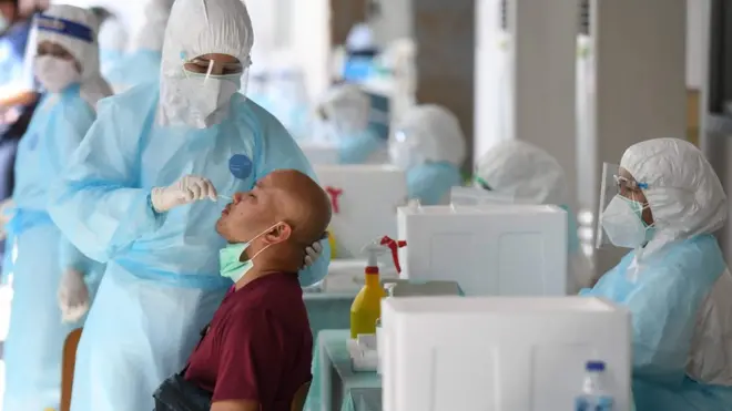 บุคลากรสาธารณสุขสวมชุดป้องกันอย่างเต็มในที่ระหว่างตรวจหาเชื้อโควิด-19 ในพื้นที่เสี่ยงสูง