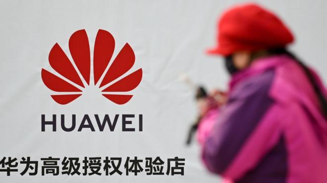 A woman uses her smartphone while walking past advertising outside a Huawei store in Beijing on January 29, 2019. -