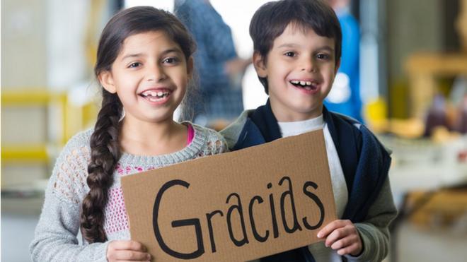 Una niña y un niño sostienen un letrero que dice Gracias.