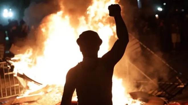 Protester stands in front of a fire with an arm raised