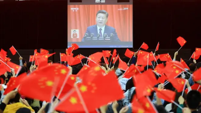 This file picture taken on 18 October 2017 shows college students waving national flags as they watch the opening of the 19th Communist Party Congress in Huaibei in China's eastern Anhui province.
