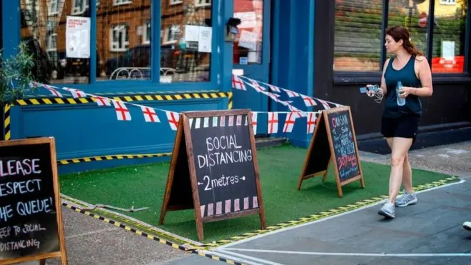 امرأة تسير أمام مطعم وضع علامات التباعد الاجتماعي بسوق بورتوبلو بلندن في الأول من يونيو/حزيران بعد تخفيف قيود الإغلاق