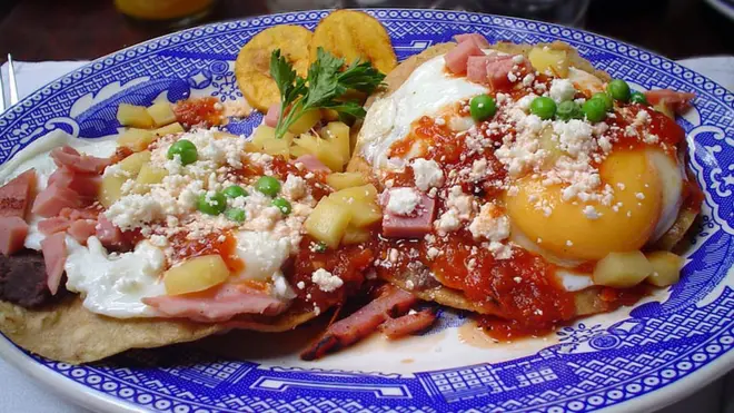 Una delicia de Yucatán: huevos motuleños, que son fritos y servidos sobre una tostada con frijoles negros, salsa de tomate, jamón y chícharos, con plátano, queso y salsa picante.