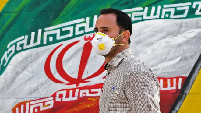 Iranian man wearing a mask in front of a mural of the national flag in Tehran (04/03/20)