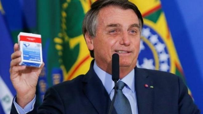 Jair Bolsonaro sorri e segura embalagemblazer com como jogarhidroxicloroquina