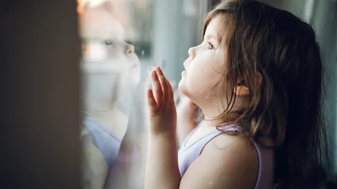 طفلة تنظر عبر نافذة وترى صورتها منعكسة