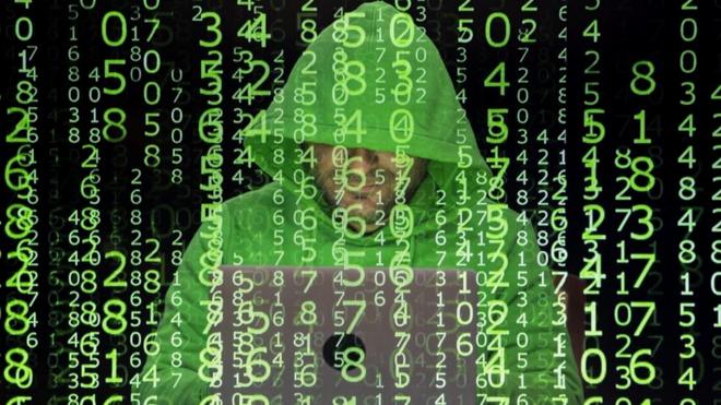 Em segundo plano, um homem anônimo em frente a um laptop, vestido com uma blusa com gorro; em primeiro plano, diversos números verdes