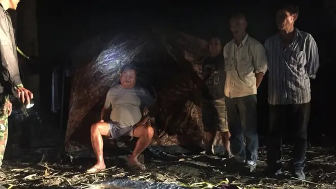 ภาพถ่ายนายเปรมชัย กรรณสูต (นั่งตรงกลาง) ขณะที่ถูกเจ้าหน้าที่เขตรักษาพันธุ์สัตว์ป่าทุ่งใหญ่นเรศวรจับกุมตัว