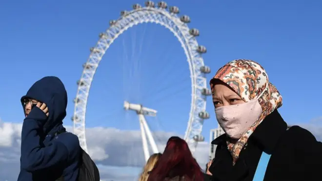 Seorang perempuan mengenakan masker berjalan melintasi Jembatan Westminster di pusat kota London, Inggris