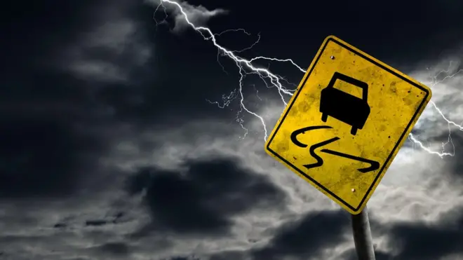 Una señal de "pavimento resbaladizo" y un rayo al fondo