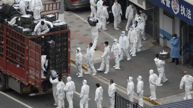 Koruma kıyafetleriyle gıda maddesi dağıtımına yardım eden işçiler