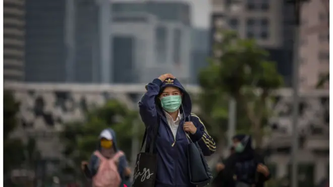 Pekerja menggunakan masker berjalan kaki di pusaat kota Jakarta pada Senin (23/03) ketika Pemprov DKI menyerukan warganya berdiam di rumah
