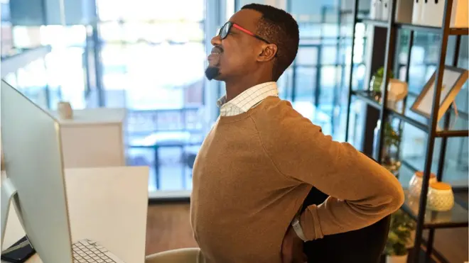 Un homme touchant son dos devant son laptop