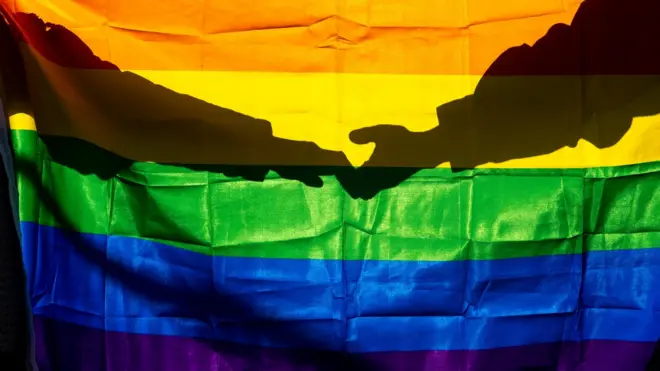 امرأتان تمسكان يدي بعضهما وأمامها علم قوس قزح