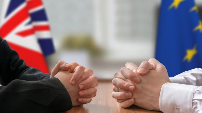 Люди за столом переговоров с флагами Британии и ЕС