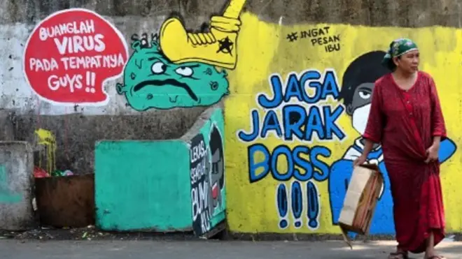 Warga melintas di depan mural berisi ajakan menjaga jarak di Jalan Pahlawan Komarudin RW 03, Cakung Barat, Jakarta Timur, Sabtu (17/10/20).