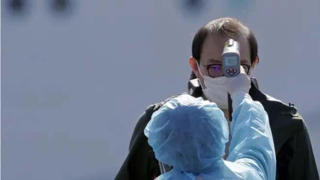 (Foto ilustrasi) Seorang pekerja berpakaian khusus memeriksa para penumpang yang baru turun dari kapal pesiar Diamond Princess yang bersandar di Pelabuhan Yohohama, Jepang.