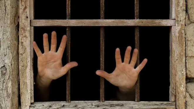 Un prisonnier passe ses mains a travers la fenêtre de sa cellule - on ne voit que les paumes de ses mains