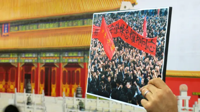 一名香港支联会示威者在中环车站故宫壁画前举起1989年学运照片（BBC中文网图片9/1/2017）