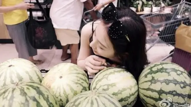 Photo of a girl wearing sunglasses and listening to a watermelon.