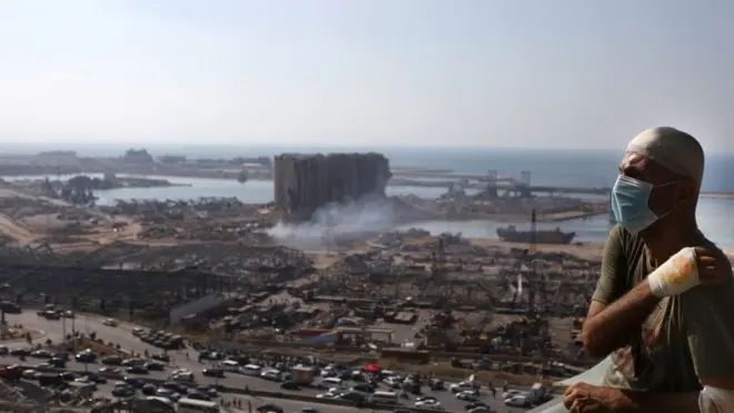 شخص مصاب بانفجار بيروت، يظهر خلفه مرفأ بيروت