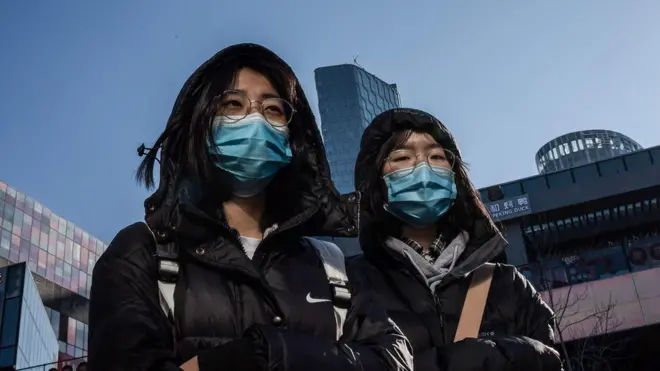 People wear protective masks as they walk outside a shopping mall in Beijing on January 23