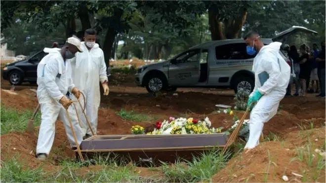 Gravediggers wear protective suits as they work during a burial
