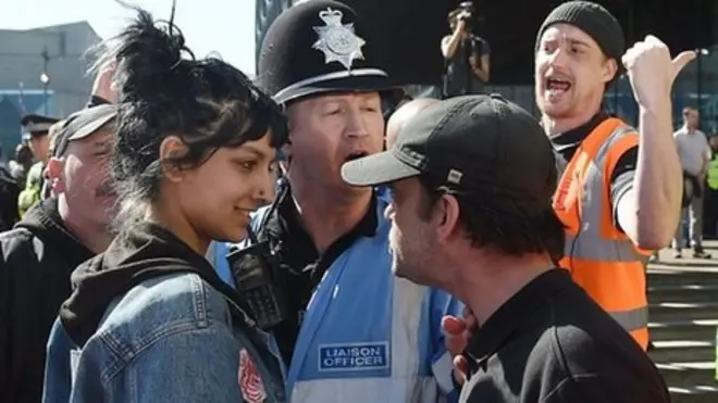 英中部のバーミンガム市で先週末、極右団体のメンバーに取り囲まれた女性を助けようと、微笑みながら割って入った若い女性の写真がソーシャルメディアで拡散され注目を集めた。