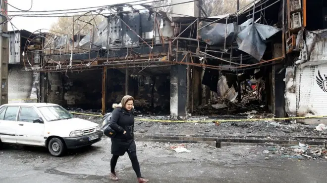 An Iranian woman walks past a shopping centre that was burned during protests over increasing fuel prices in the city of Shahriar, Alborz province, Iran, 20 November 2019.