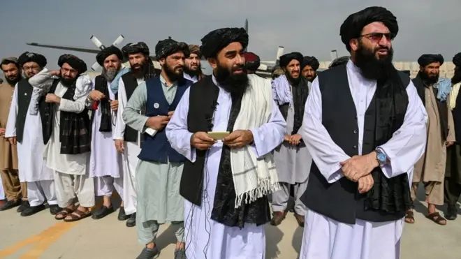 Juru bicara Taliban, Zabihullah Mujahid, (tengah, memegang kertas) dengan pimpinan lainnya saat berbicara ke media massa di Bandara Kabul 31 Agustus 2021.