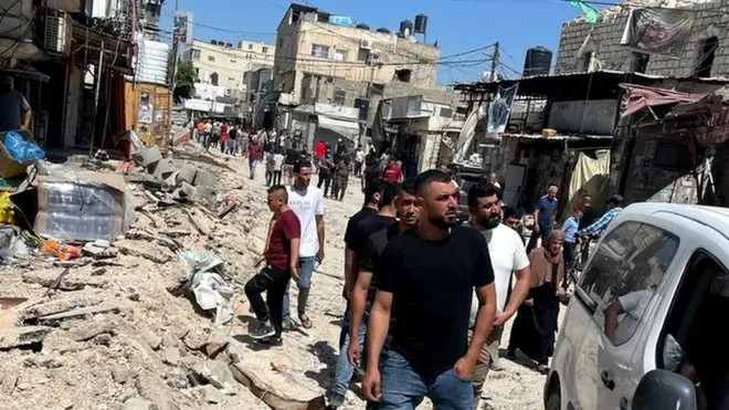 Palestinians inspect damaged vehicles, roads and vehicles in Jenin refugee camp, in the occupied West Bank, following a major Israeli military operation (5 July 2023)