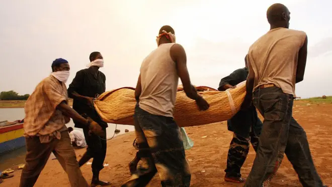 Some men wey carry wrapped body of one victim of one sinking boat for lake Volta, 11 April 2006 for Tapa Popoassy village.