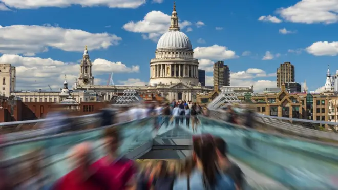 Time-lapse image depicting pedestrians in motion on the Millennium Bridge